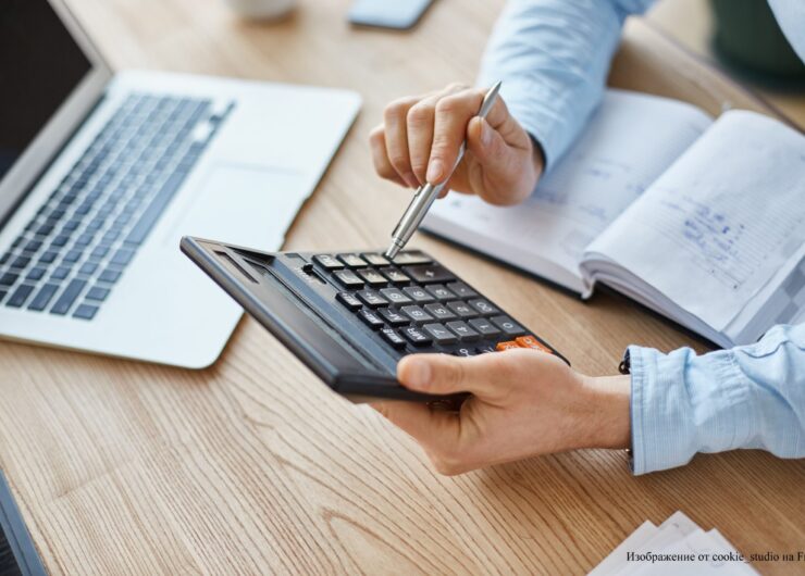 Cropped view of professional serious finance manager, holding calculator in hands, checking company month's profits, looking through details on laptop, writing down information for meeting with director